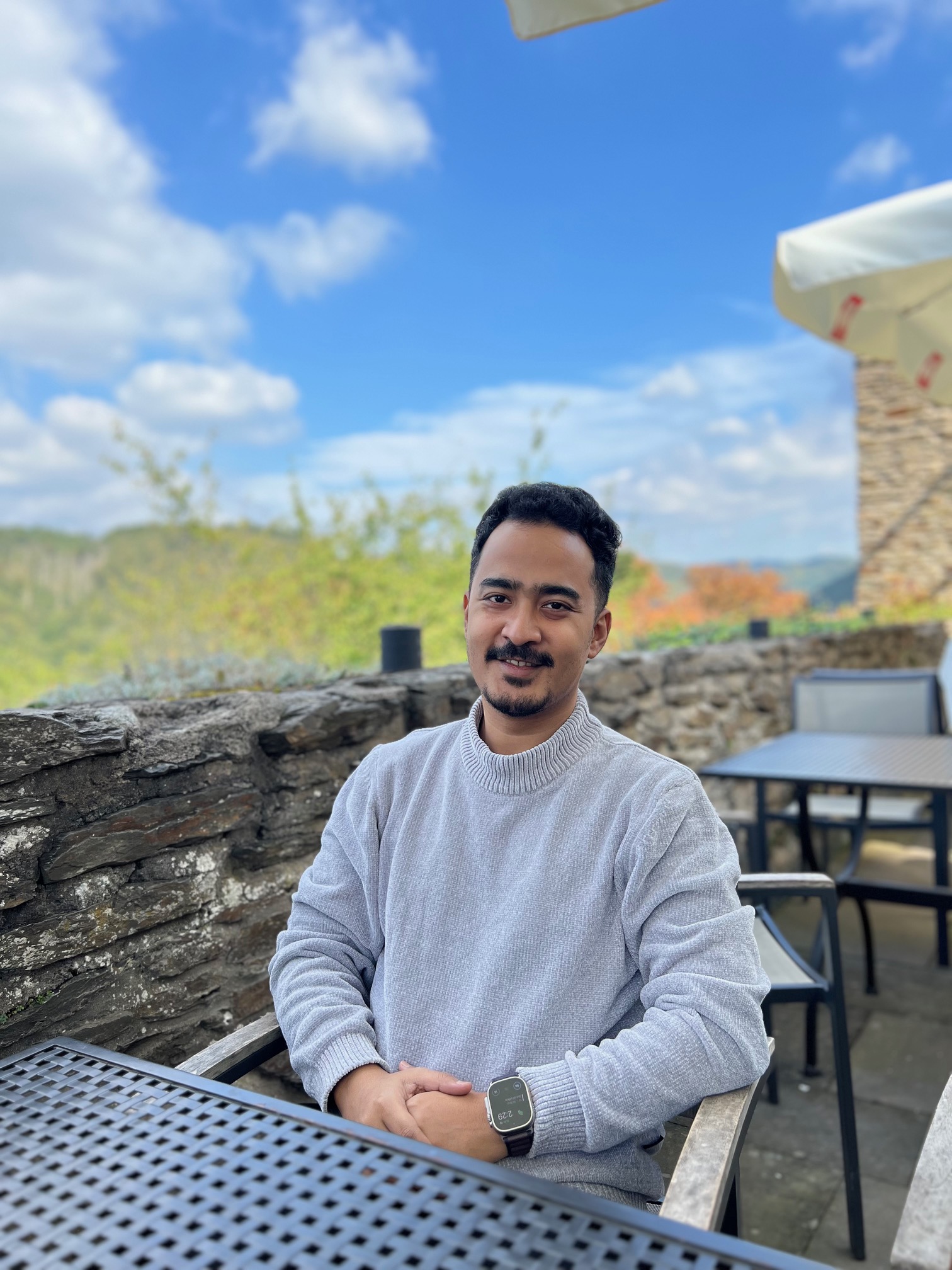 Abhinav, sitting at an outdoor cafe with a hillside view